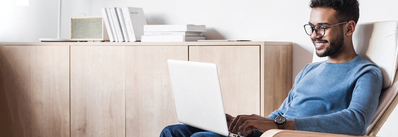 Hombre joven sentado en un sillón que navega por la web con una computadora portátil