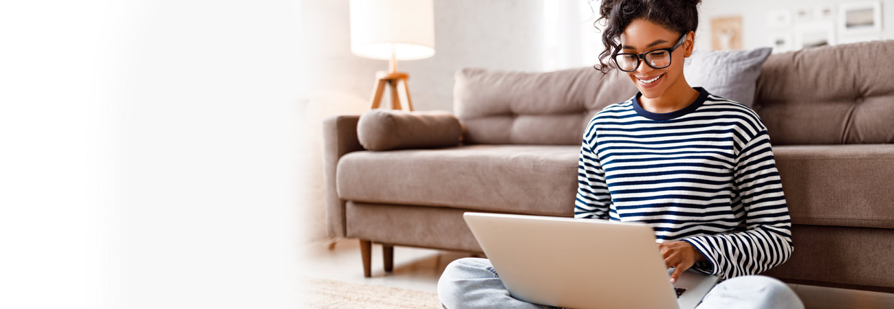 Woman sitting beside couch smiling at laptop computer