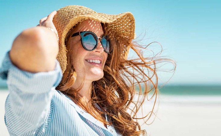 Woman sitting on beach holding onto sun hat