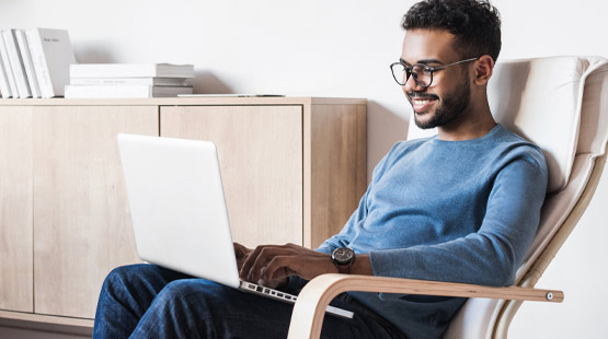 Young man sitting on armchair browsing the web on a laptop Young man sitting on armchair browsing the web on a laptop