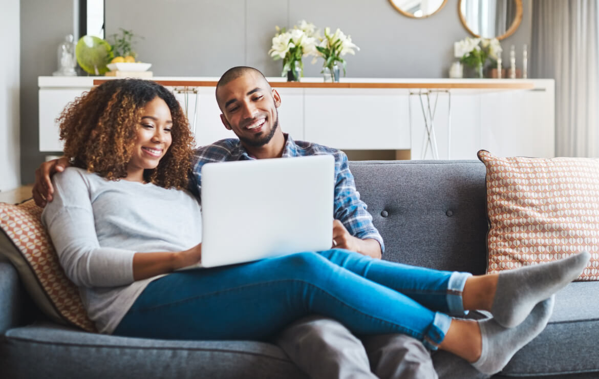 Young couple sitting together on couch looking at laptop