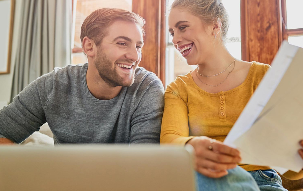 Couple smiling together while viewing document and laptop