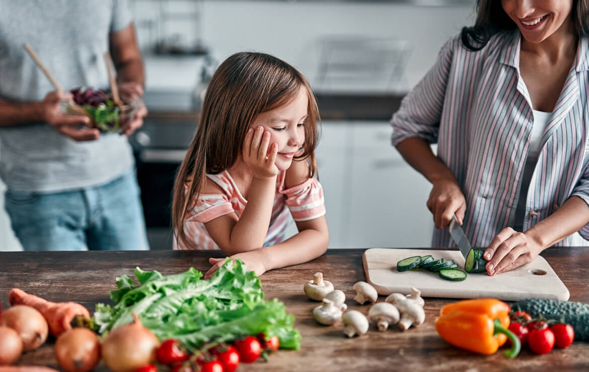 Daughter watching mother cut vegetables in kitchen