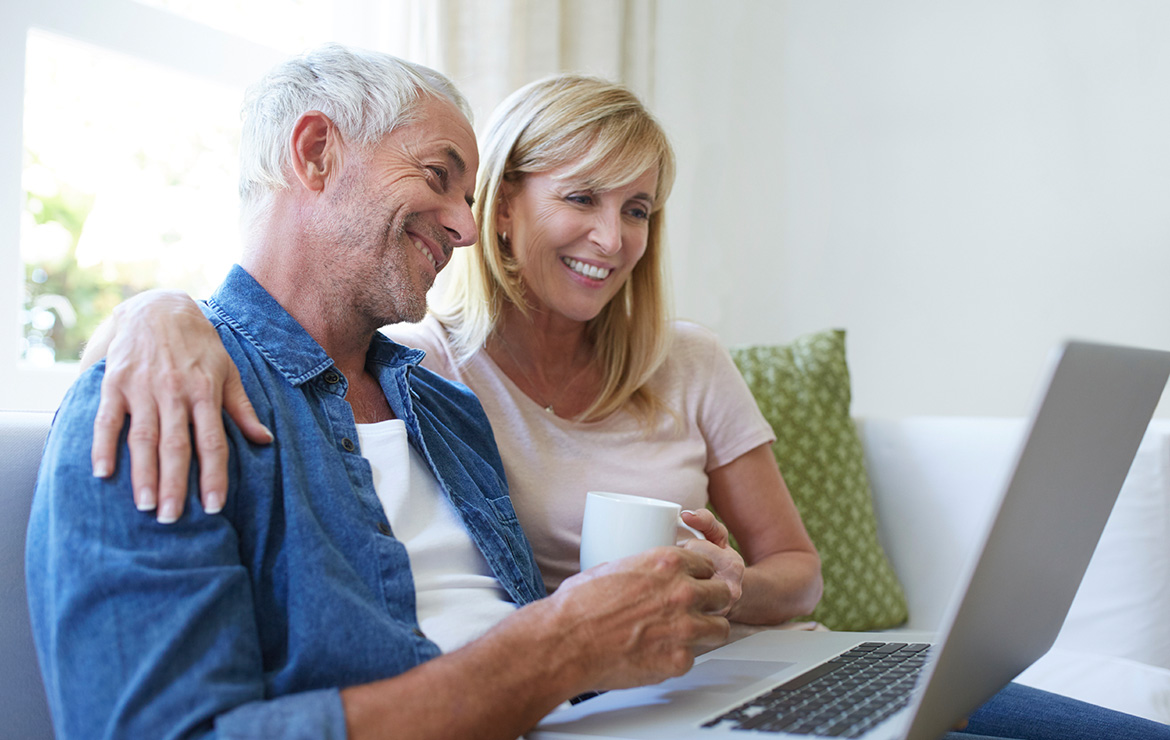 Elderly couple drinking hot beverage using laptop