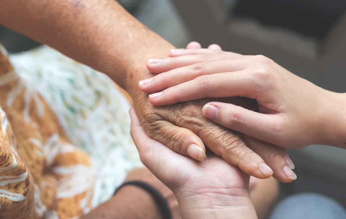 Elderly hand being held by younger hands