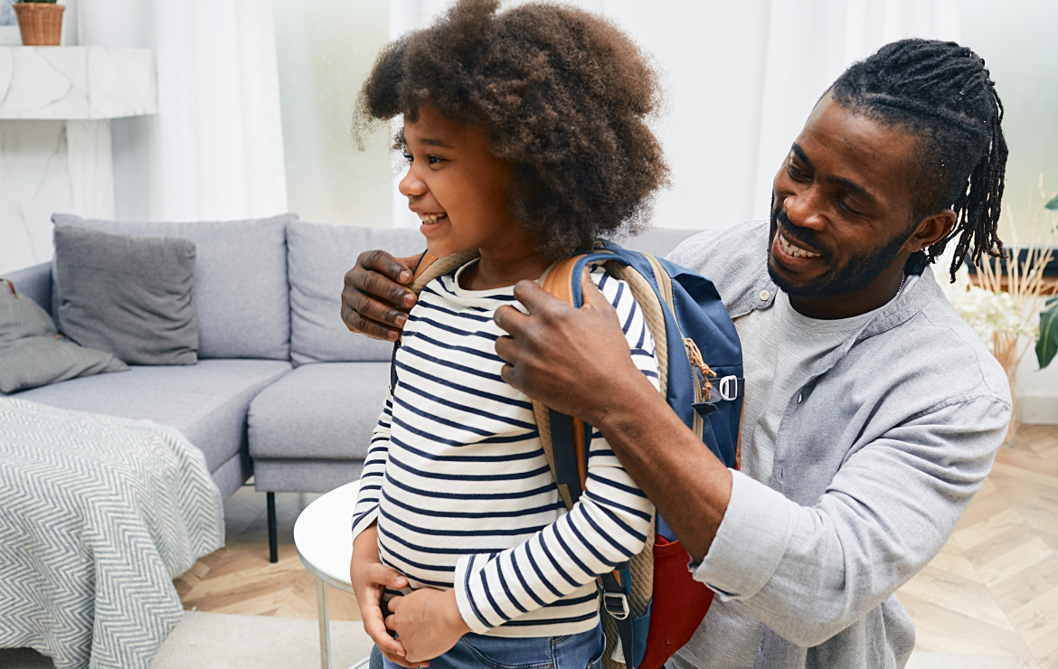 Father helping daughter put on backpack