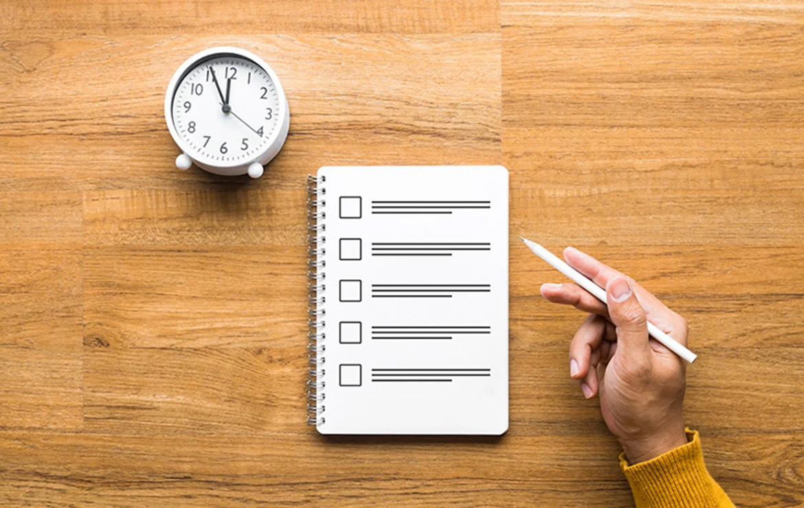 Hand holding pen next to notebook and clock