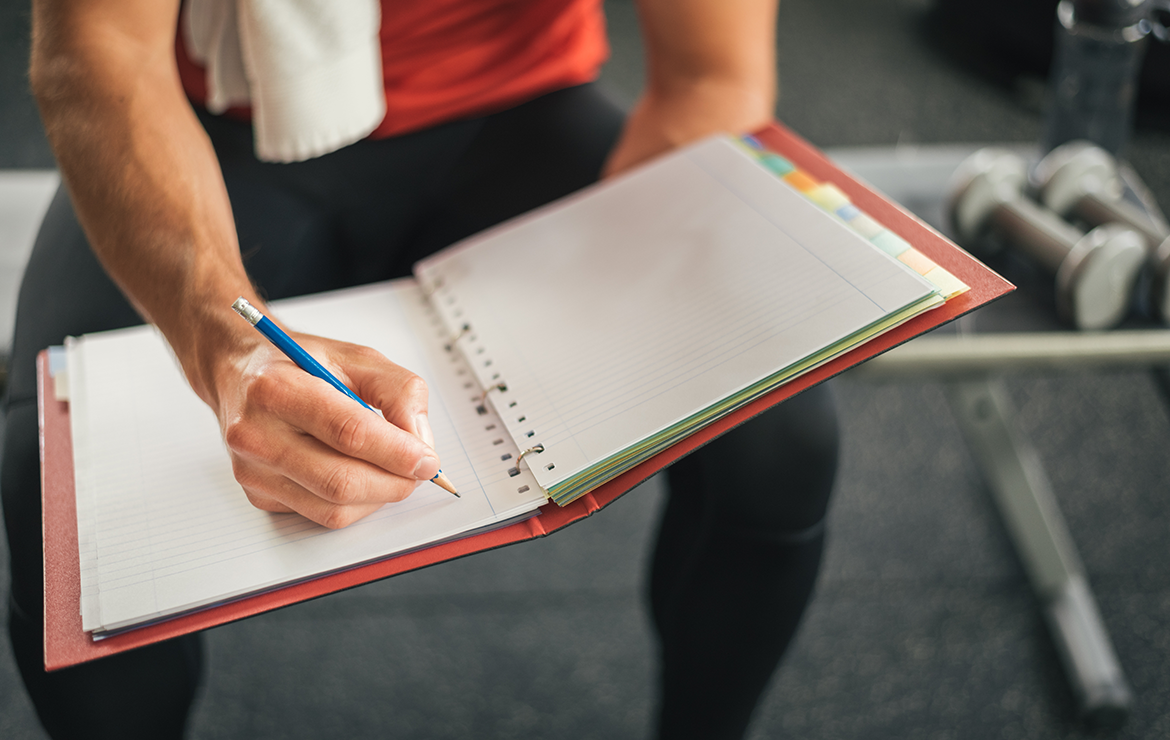 Man sitting at gym writing on notebook