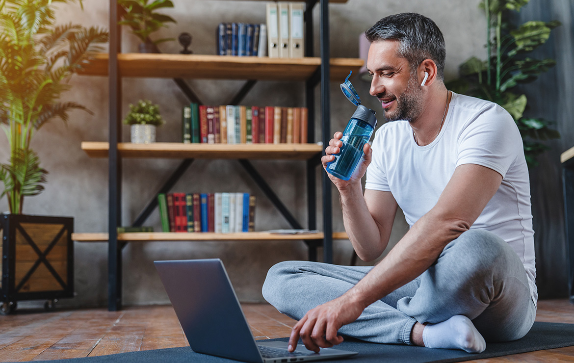 Man sitting down drinking water and using laptop