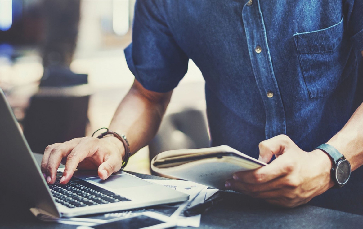 Man using laptop while holding documents