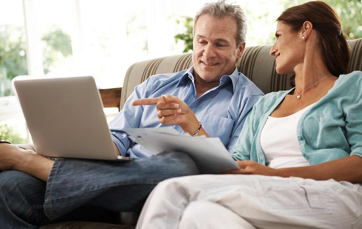 Middle-aged couple holding document and viewing laptop