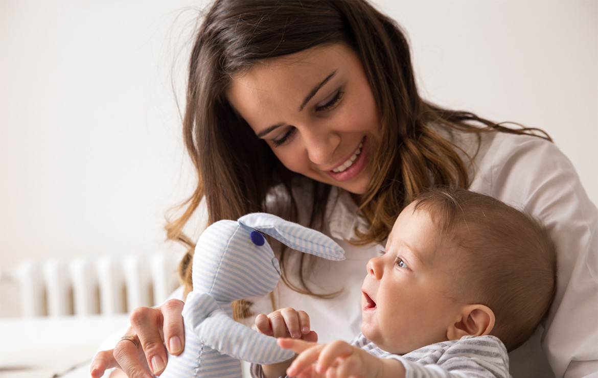 Mother holding stuffed animal in front of baby
