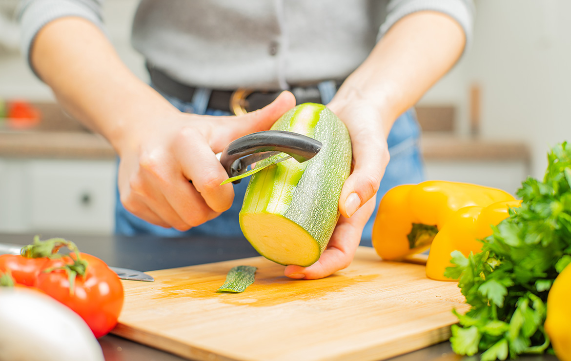 Peeling zucchini on top of cutting  board