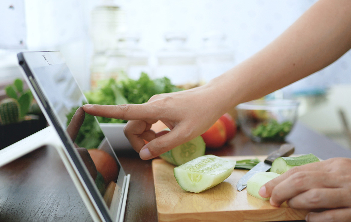 Person cutting vegetables and tapping on tablet