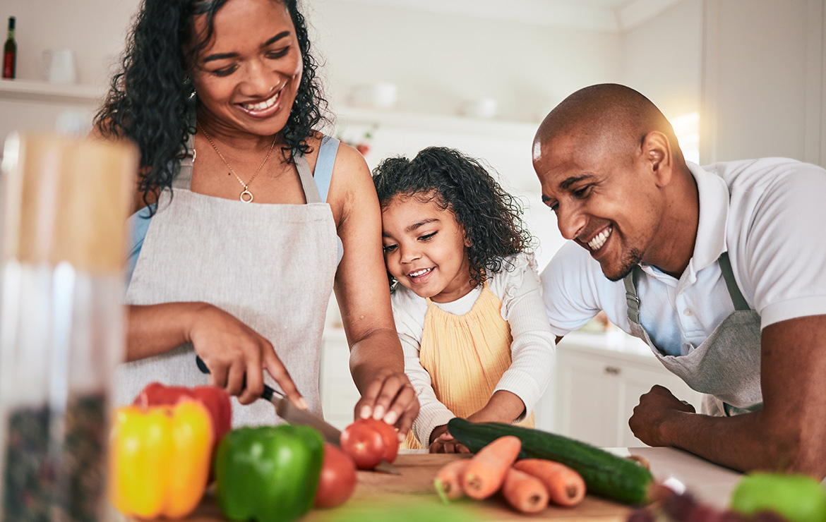 Smiling parents and child chopping vegetables