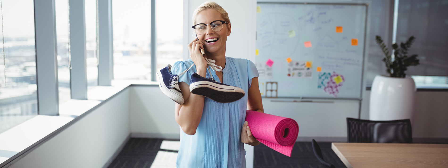 Woman smiling on the phone while holding yoga mat and sneakers
