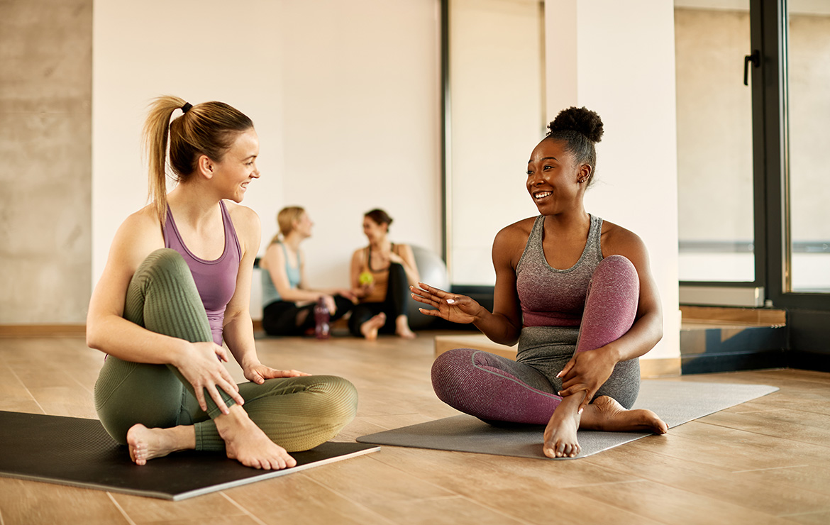 Two women smiling at each other while sitting on yoga mats