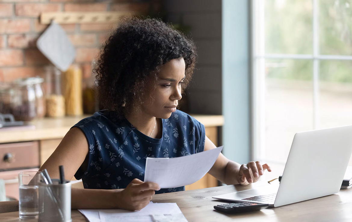 Woman holding document and typing in laptop