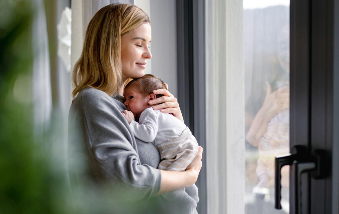 Mother holding newborn child by window