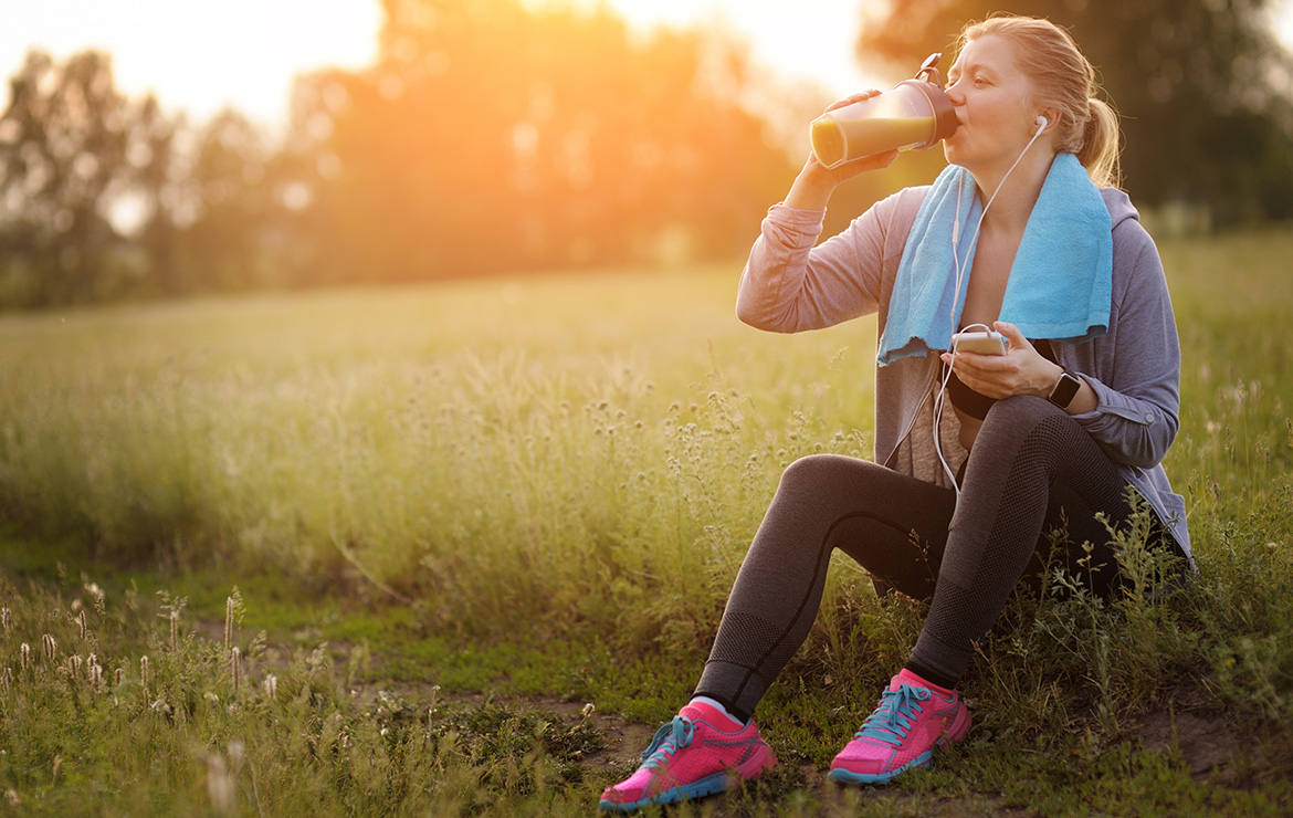 Woman in workout clothes drinking shake at park