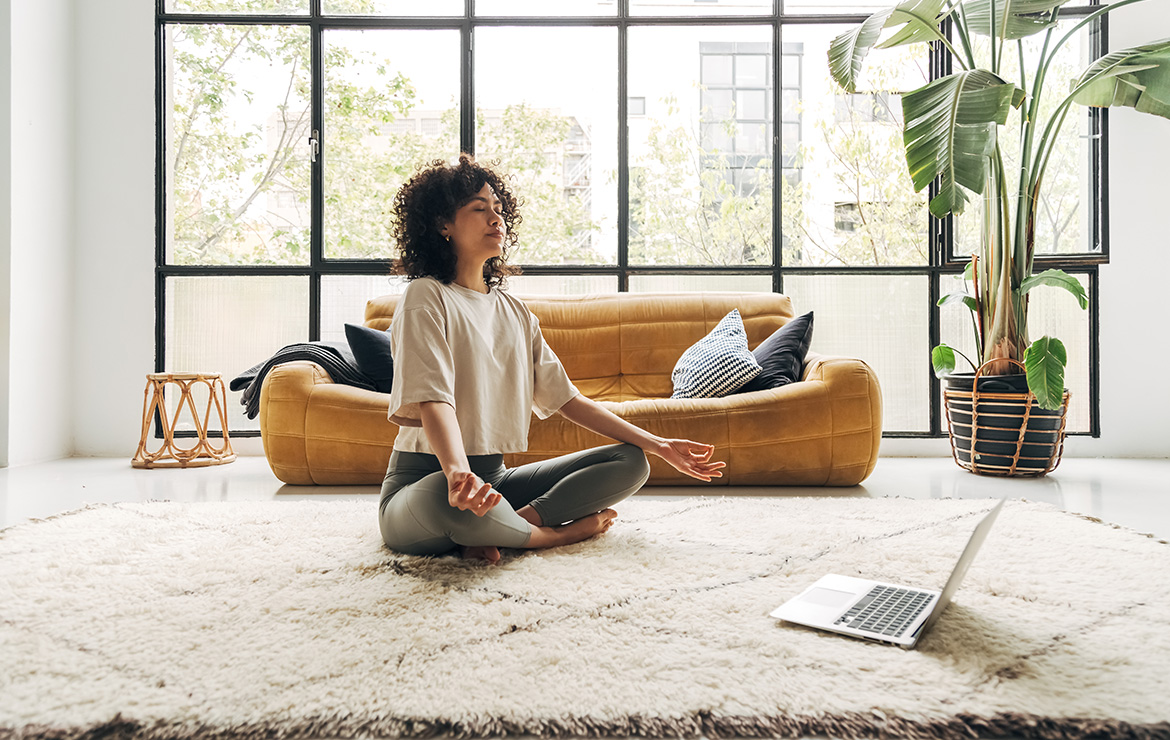 Woman meditating at home in front of laptop