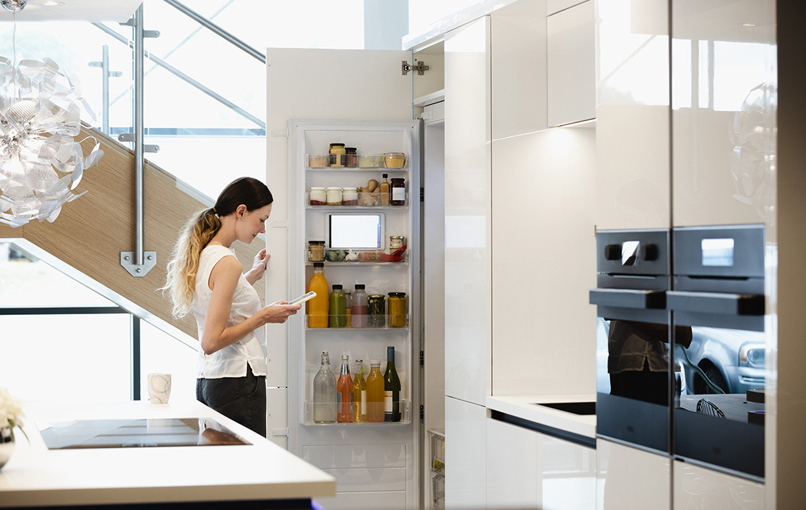 Woman opening fridge while viewing smartphone