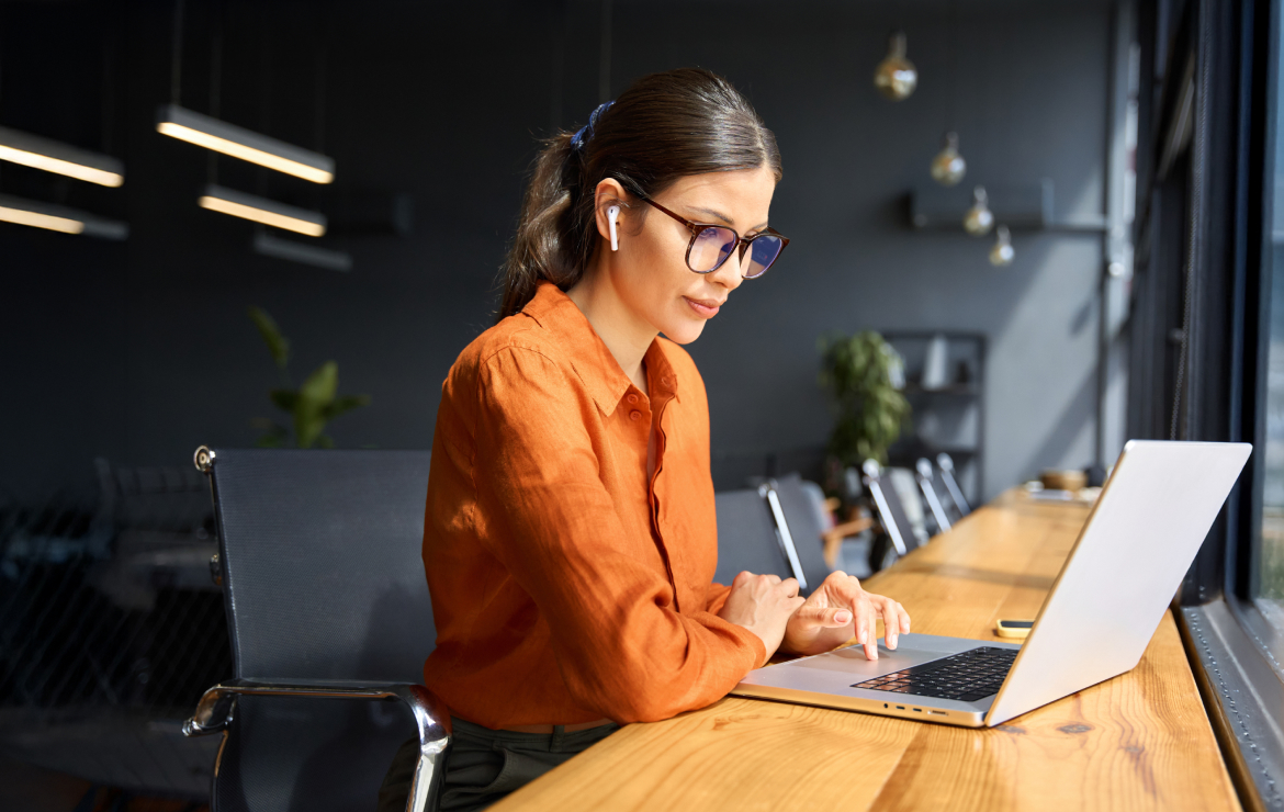 Woman wearing earphones scrolling on laptop in office