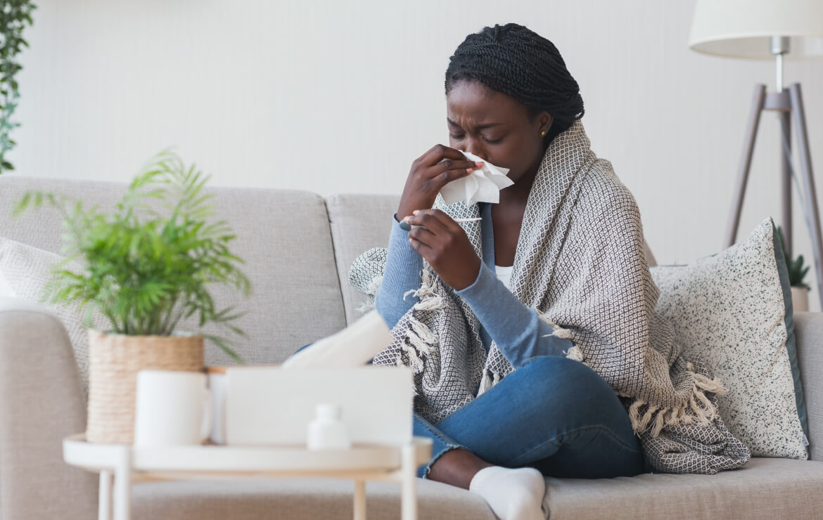 Woman sitting on couch sneezing into tissue