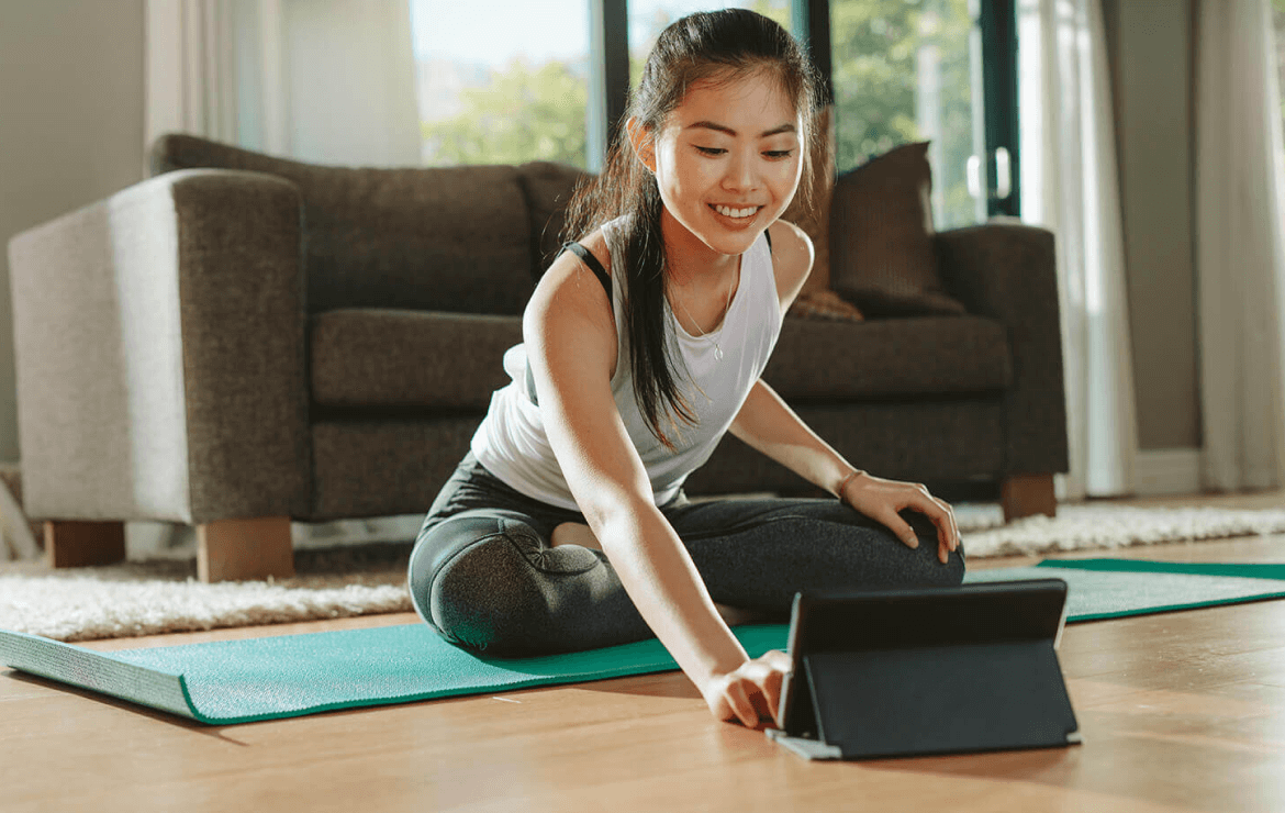 Woman sitting on yoga mat in living room scrolling on tablet