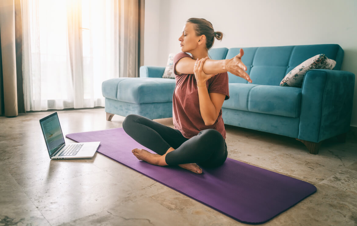 Woman sitting on yoga mat stretching out arm