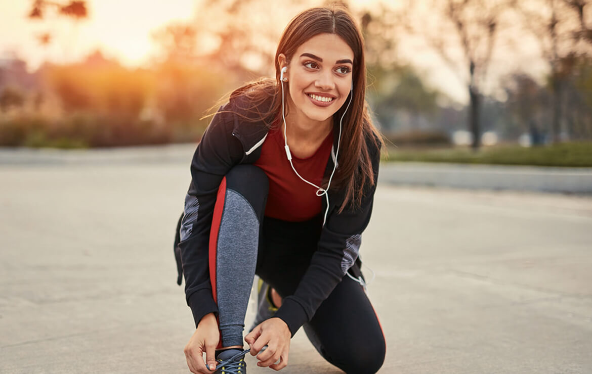 Woman wearing earphones tying shoes before run