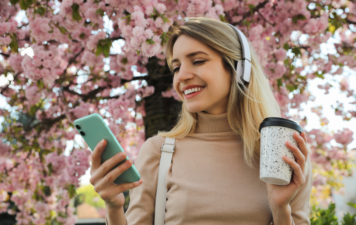 Woman wearing headphones smiling while holding mobile phone and coffee