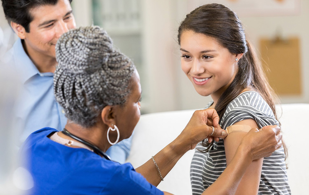 Young woman receiving band aid in arm from nurse