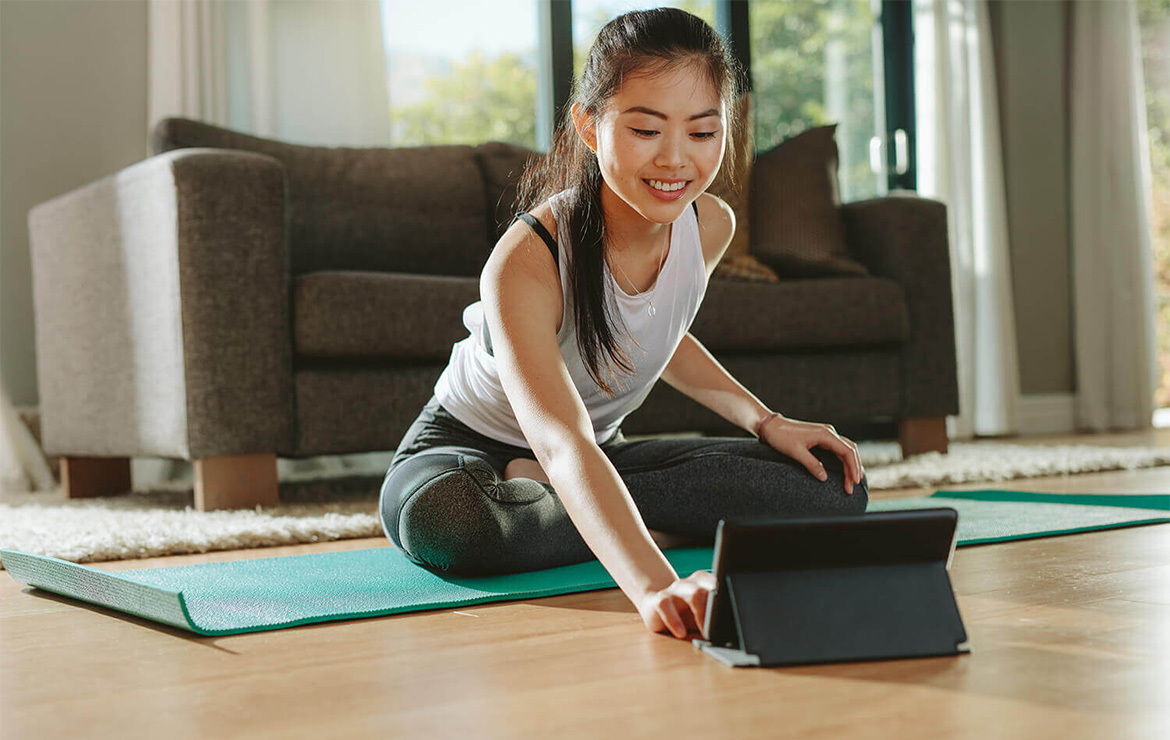 Young woman sitting on yoga mat using tablet