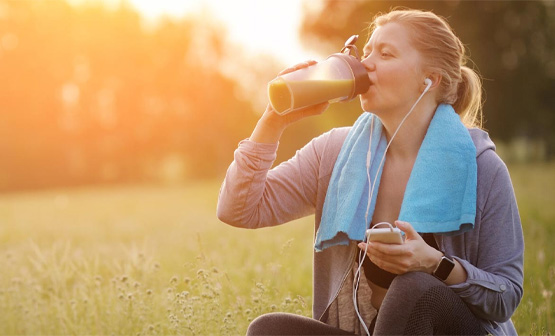 Woman wearing earphones sitting on grass drinking from water bottle
