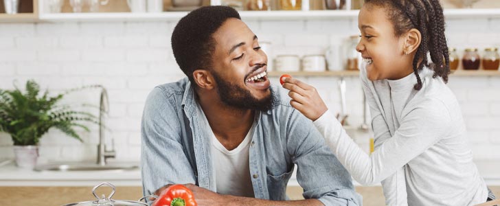 Father and daughter eating vegetables together in the kitchen