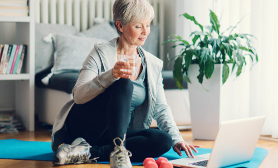 Older woman viewing laptop while exercising with weights