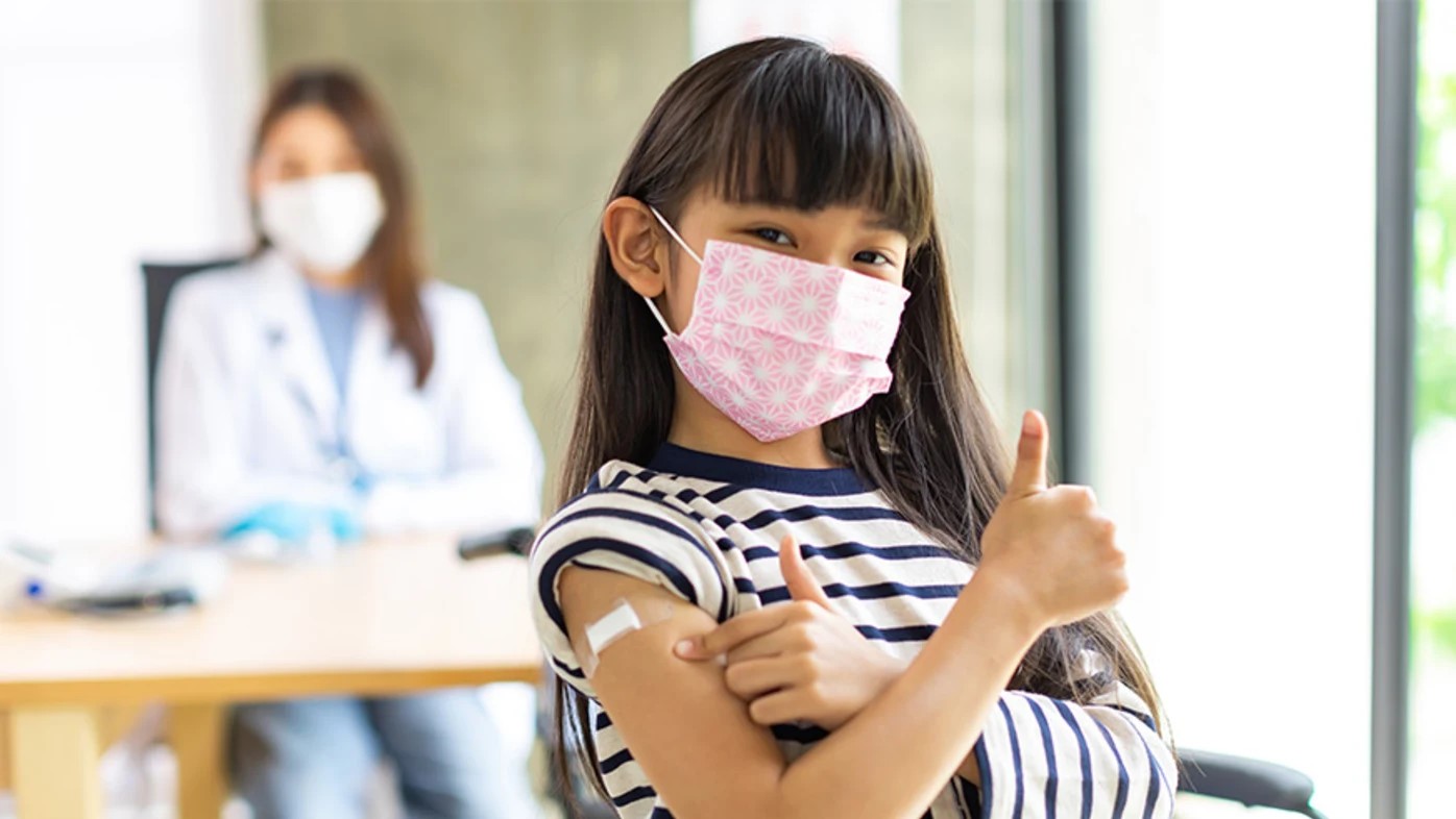 Young girl wearing mask giving thumbs up after receiving vaccine